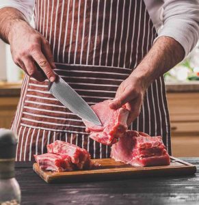 Boucher entrain de découper de la viande sur une planche en bois